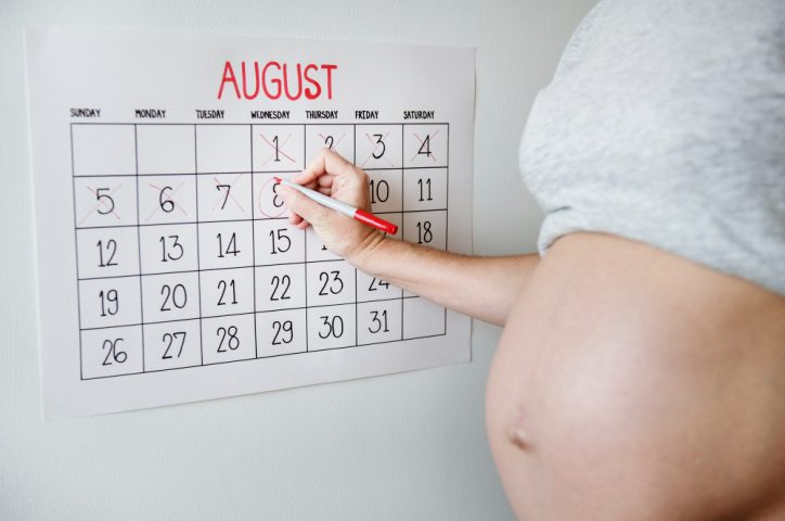 une femme enceinte qui écrit sur un calendrier mural